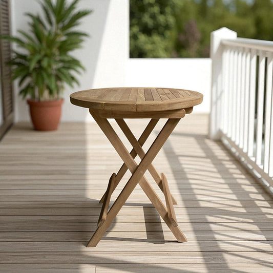 Cilacap folding round table made of teak wood, placed on a sunlit outdoor deck with white railing and potted greenery in the background