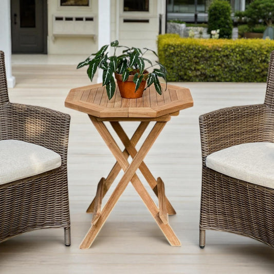 Teak wood Cilacap Side Table with octagonal top, styled between two wicker chairs on a wooden patio, surrounded by lush potted plants and glass-panelled doors—ideal for outdoor relaxation.