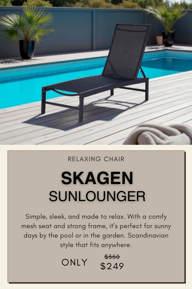 Black Skagen sunlounger on wooden deck beside pool, surrounded by greenery and brick wall in background.