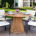 Nusa Dua round wooden outdoor dining table with slatted base, styled with white tableware and floral centerpiece on a garden patio deck.