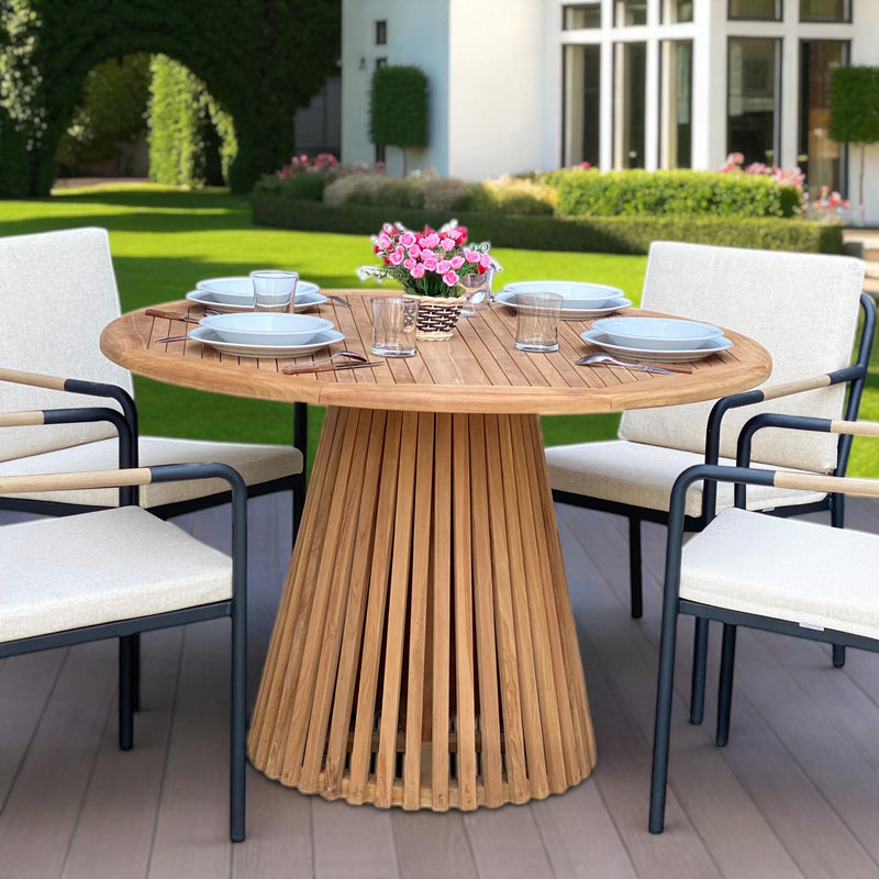 Nusa Dua round wooden outdoor dining table with slatted base, styled with white tableware and floral centerpiece on a garden patio deck.