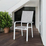 Pisa Outdoor Dining Chair with white aluminum frame and grey sling fabric seat and backrest, placed on a wooden patio beside a potted plant and modern building wall.